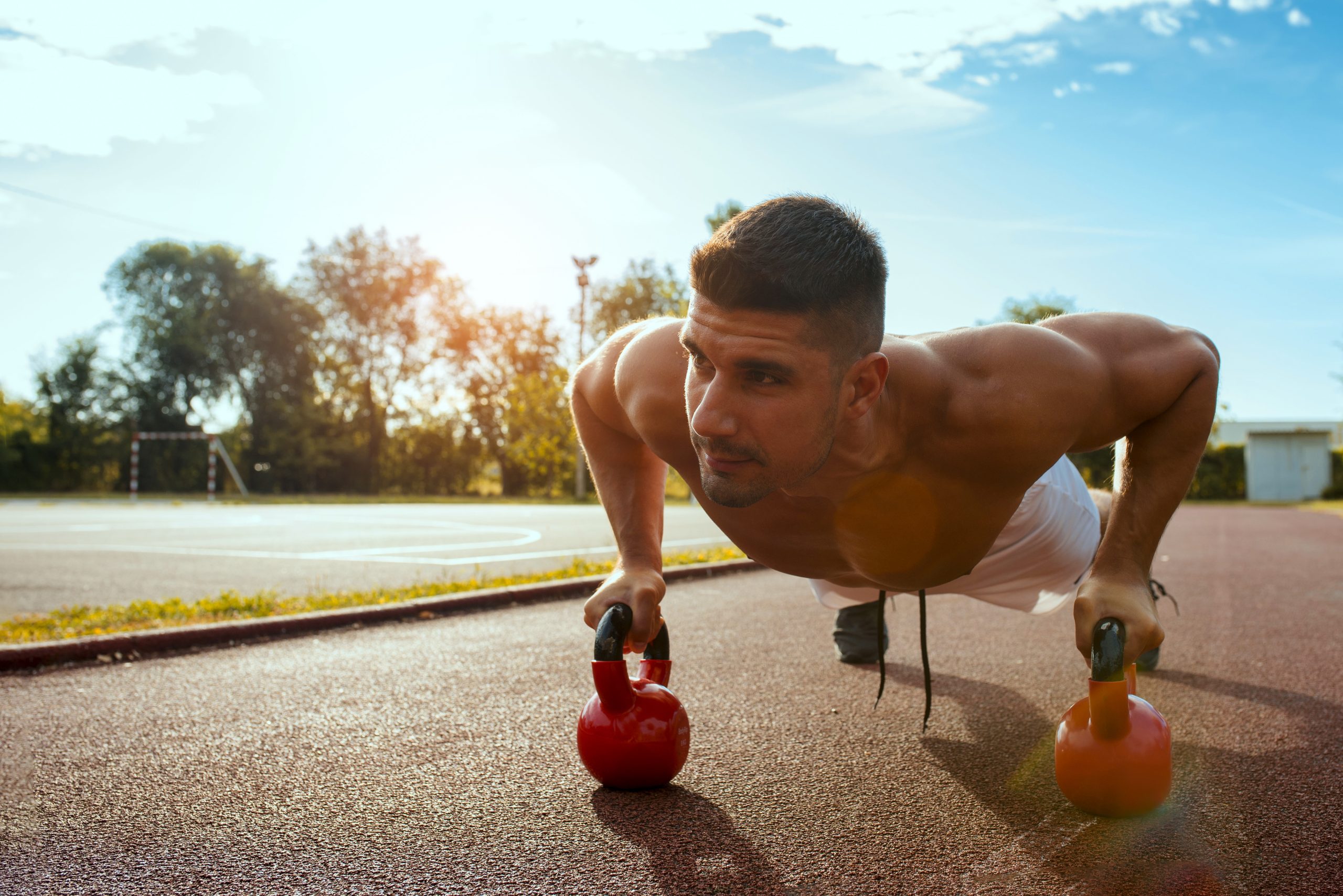 A young shirtless Caucasian male working out in the park at daytime